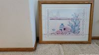Landscape-oriented framed artwork featuring blue cactus, Southwestern pottery, and desert landscape on floor against wall.