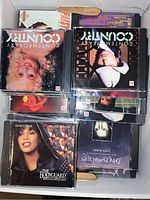 Top view of several CD jewel cases in a file box showing covers including country music albums and The Bodyguard soundtrack by Whitney Houston and Kevin Costner.