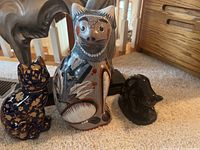 Three porcelain cat figurines in front of a horse sculpture