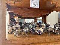 Group of thirteen cat figurines on wooden shelf, each wearing Native American style feathered headdresses and clothing.