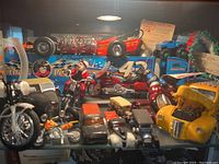 Photo of diecast cars and motorcycles in display. Includes various models including a red dragster, blue truck with race number, yellow vintage car, and multiple motorcycles along with a trading card insert.