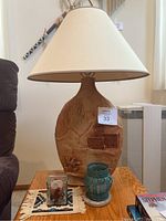 Lamp with a large ceramic base featuring embossed southwestern design and cream colored fabric shade with wide brim.