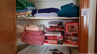 Shelf with neatly folded towels in green, navy, teal, beige, pink, and red. Several boxed puzzles stacked including a 1000-piece and 500-piece puzzles.