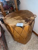 Large wooden side table shaped like a drum with animal hide top and rope decorative elements on the sides