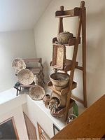 Photo showing wooden leaning shelf unit with woven baskets placed on shelves along with pottery and small crafts.