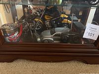 Full view of the glass case containing the collectable motorcycles, radio control car and metal cup showing assembled group of items.