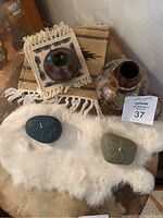 Photo showing two Native American style small vases or jugs, two carved candles placed on white fur, and a small patterned woven textile underneath one vase.