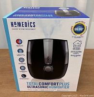 Box of HoMedics TotalComfort Plus Ultrasonic Humidifier showing brand, model, features, and key information about warm/cool mist, 1.4 gallon tank, coverage area 547 sq. ft., auto-off timer, and Clean Tank Technology.