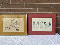 Two bathroom art prints displayed side by side against a brick wall; left print framed, right print in glass and matte only.