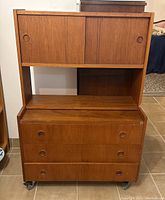 Front view of teak bookcase showing three drawers with recessed circular handles below an open area and upper sliding doors with circle cut handles.