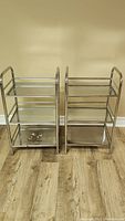 Front view of two chrome-finished metal racks side-by-side showing three perforated shelves each.