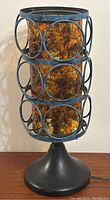 Front view of the lamp showing the cylindrical amber glass shade with blue-gray metal circular frame and black base.