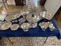 Full view of all silver plate items arranged on table showing variety of bowls, trays, condiment holders, and chafing dish.