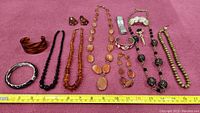 Full view of all jewelry items laid out on pink fabric with tape measure for size reference.