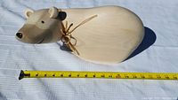 Side view of the carved polar bear sculpture on a white fabric with measuring tape showing about 14 inches length.