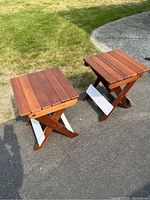 Two small wooden foldable tables placed outdoors, showing tops and side profiles