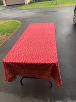 Photo showing the red patterned tablecloth spread over a rectangular table outdoors, highlighting its full size and pattern.