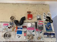Wide view of assorted plumbing items neatly arranged including valves, fittings, PVC pipes, washers, and hardware on a wooden surface.