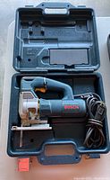 Opened carrying case showing Bosch electric jigsaw inside with power cord neatly coiled.