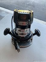 Front view of the Craftsman router showing the power switch and side handles with power cord coiled around base.