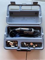 Gray plastic carrying case open showing Dremel rotary tool and accessories inside.