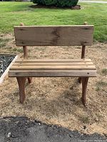 Front view of small wooden garden bench decoration on grass, showing backrest and slatted seat.