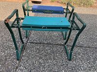 Two green metal gardening kneeler seats with blue cushions on a stone surface. Front seat shows damage on the left arm support.
