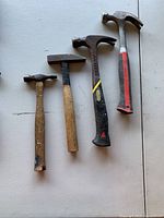 Four claw hammers laid out on a flat surface, showing wood and composite handles with visible wear