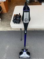 Full view of upright Hoover Fusion cordless stick vacuum and charging base on a table and floor