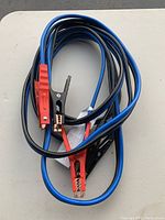 One photo showing a coiled pair of jumper cables with red and black clamps on a white surface.