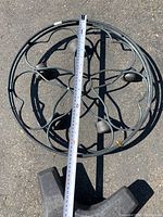 Top-down photo showing a round metal plant stand with four caster wheels and a measuring tape laid across the diameter, measuring approximately 22 inches.