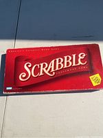 Top view of closed Scrabble game box showing red cover with Scrabble logo and yellow corner sticker.