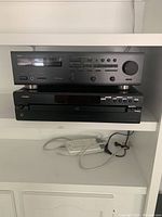 Yamaha stereo receiver stacked on Denon 5-disc CD player on a white shelf with power strip below