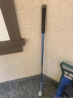 Watering wand leaning against a textured wall, showing full length and grip details.