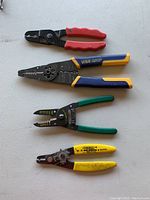 Photo showing four assorted wire crimping and stripping tools on a flat surface, each with different colored handles and design variations.