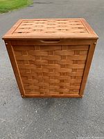 Front view of the wooden laundry hamper showing woven panel design and handle groove on top lid