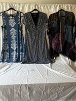 Image of two dresses and a shawl on hangers against a light backdrop for display.
