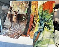 Three shower curtains displayed hanging over a table, visible prints of deer, autumn trees, and a parrot.