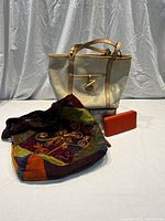 Photo showing all three items: a large cream canvas purse with tan leather trim and toggle closure, a colorful patchwork fabric purse with embroidery, and an orange wallet.