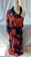 Full front view of the one shoulder black and orange floral print dress displayed on a dress form, showing sleeve and elastic waist.