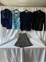 Five women's clothing items displayed on hangers and laid flat including blouses, a jacket, and a skirt.