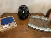 Photo shows Weight Watchers digital kitchen scale, Taylor digital bathroom scale, and Honeywell black humidifier on a brown table.