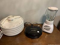 Photo of Nesco dehydrator stacked trays, Proctor Silex sandwich maker, and Oster blender on a brown table