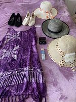 Photo showing three women's hats, purple cover-up, two pairs of shoes, sunglasses case and sunscreen pen laid on a pinkish-purple surface