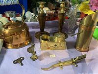 Photo showing assorted brass and copper items including candlesticks, crocodile clip, brass key, and brass containers.