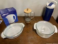 Lot items arranged on table: two casseroles with glass lids, glass coffee press, blue thermos, Kenwood electric kettle boxed