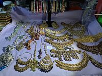 Top-down view of various Indian style costume jewelry items including necklaces, earrings, bangles, and headpieces arranged on a purple cloth.
