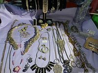 Overview of assorted crystal and rhinestone jewelry on lavender cloth, showcasing necklaces, earrings, bracelets, and brooches in silver and gold tones.