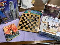 Photo showing 3D Tower puzzle box, wooden checkers and tic tac toe board with game pieces, glass chess set box with chess pieces and chess instruction book, paperback book Gulliver's Travels