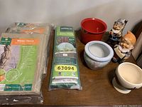 Overview image showing packaged winter fleece and grow cloche, red metal planter, and two garden dwarf statues along with ceramic planters.